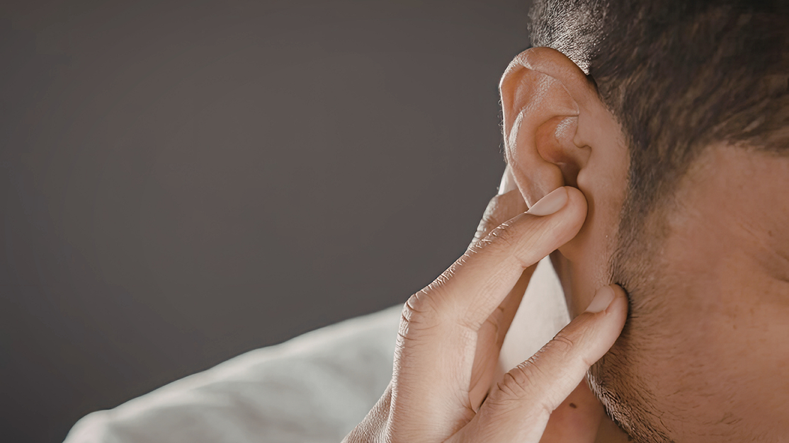 Close-up of a person touching their ear with two fingers, suggesting ear discomfort or checking the ear.