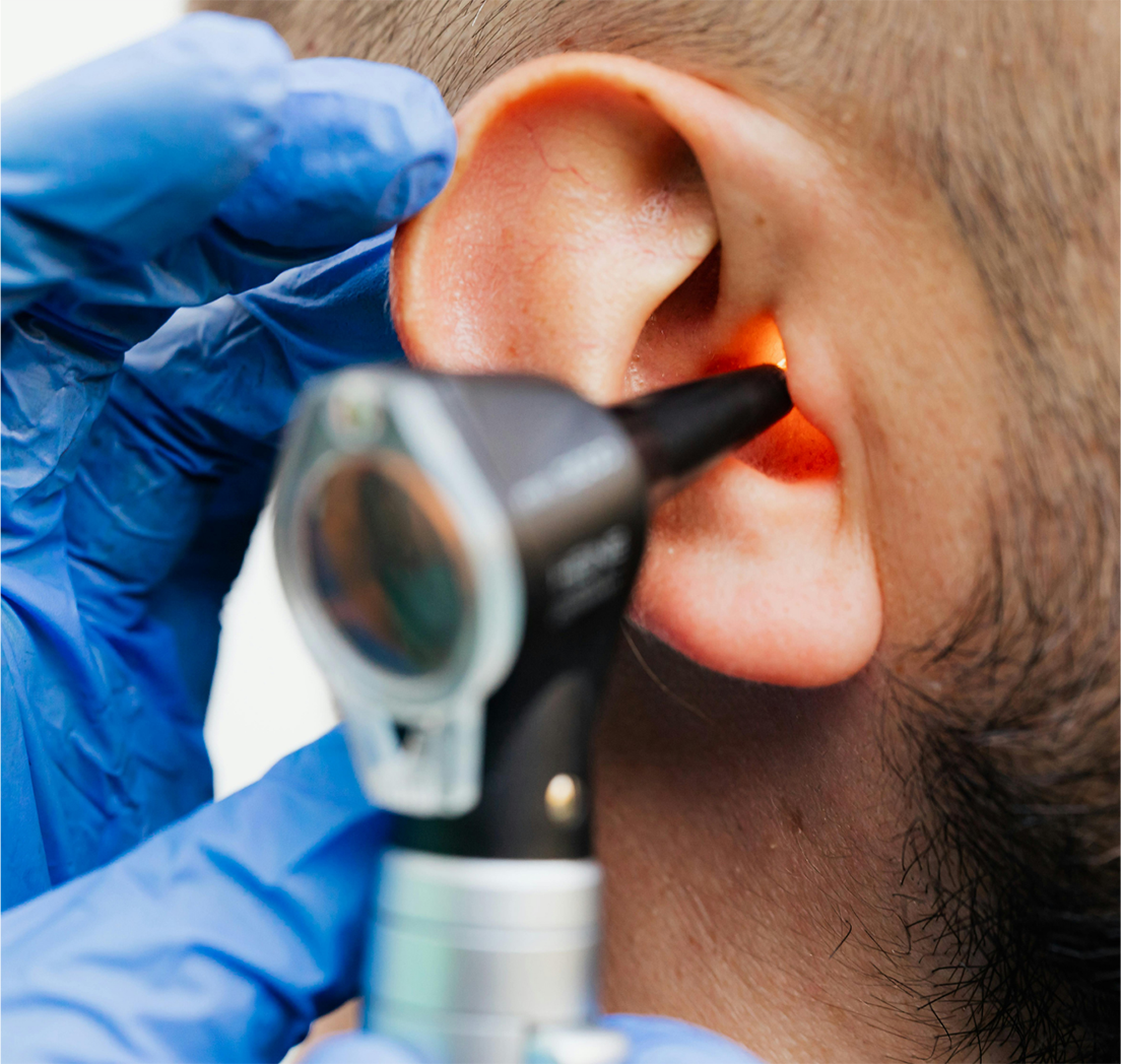 Healthcare professional in blue gloves examining a patient’s ear with an otoscope.