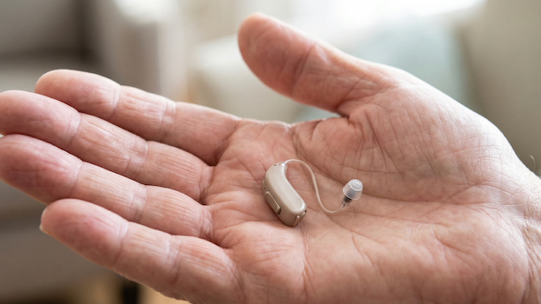 Hand holding a small behind-the-ear hearing aid (BTE) with clear tubing resting in the palm